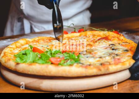 Primo piano di uno chef in guanti affettando la pizza il tagliere Foto Stock