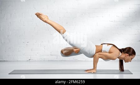 Vista laterale della donna che si bilancia sulle mani mentre si pratica lo yoga vicino a parete bianca Foto Stock