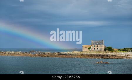 Arcobaleno sul mare e vecchia casa in pietra, giorno nuvoloso in estate, Bretagna (Francia) Foto Stock
