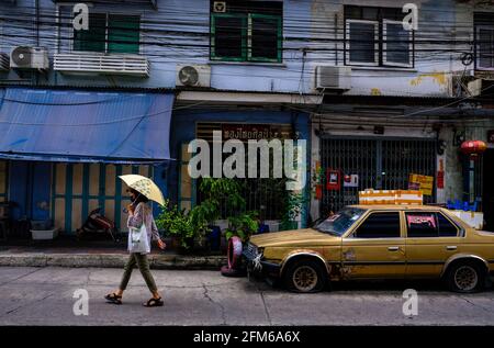 Una donna che tiene un ombrello cammina davanti a una vecchia Toyota nella zona di Chinatown a Bangkok, Thailandia. Foto Stock
