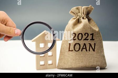 Borsa di denaro con l'iscrizione prestito 2021 e una casa di legno. Ipoteche e tassi di interesse sul bene immobile. Mercato immobiliare. Prestiti PPP. Credito. Affari Foto Stock