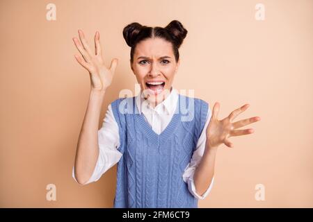 Foto di arrabbiata giovane signora pazza indossare gilet blu urlando braccia in aumento isolato sfondo di colore beige Foto Stock