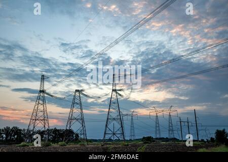 Piloni elettrici e linee elettriche ad alta tensione su sfondo tramonto. Silhouette di gruppo delle torri di trasmissione. Foto Stock