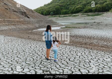 Una donna e una ragazza si levano in piedi, mano in mano, su terra asciutta e spaccata e guardano il lago, che sta asciugandosi in su. Riscaldamento globale. Foto Stock