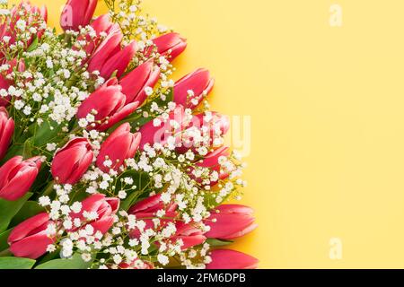 Tulipani rosa e fiori di gypsophila bouquet su sfondo giallo, fuoco selettivo. Festa della mamma, concetto di festa di compleanno. Vista dall'alto, spazio di copia Foto Stock