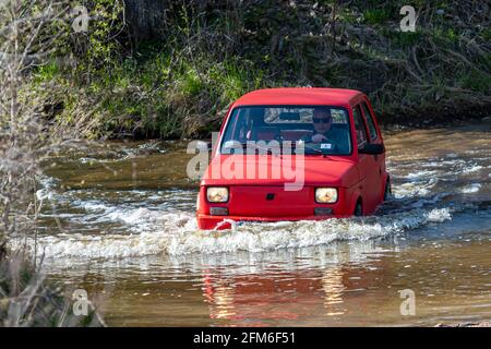 Madona, Lettonia - 01 maggio 2021: La Fiat 126, una vettura rossa a tempo indolo, supera l'ostacolo all'acqua Foto Stock