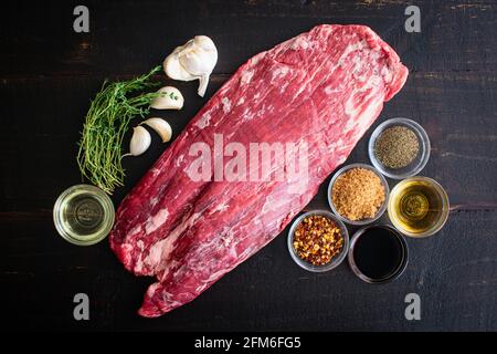 Bistecca alla griglia marinata al bourbon ingredienti: Bistecca cruda, erbe e altri ingredienti su sfondo di legno scuro Foto Stock