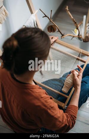 Vista posteriore di giovane donna che prepara telaio per la tessitura della lana Foto Stock