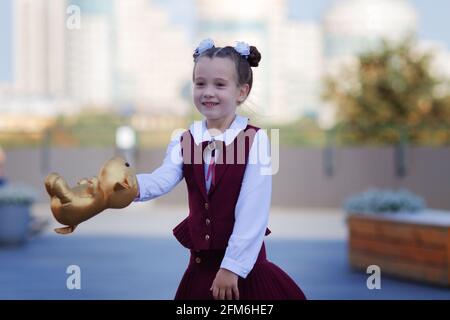 Adorabile bambina da scuola che indossa un'elegante uniforme danzante con il suo mouse dorato preferito all'aperto nel cortile della scuola Foto Stock