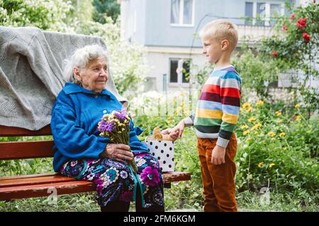 bisnonna di 90 anni, nonna con nipote insieme. Nipote abbraccia la sua amata nonna. Il nipote di capretto è venuto alla nonna con il fiore Foto Stock