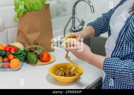 Perdita di cibo e spreco di cibo. Ridurre gli sprechi alimentari a casa. Risolvere il problema dei rifiuti alimentari. Le mani femminili pelano le patate, la buccia di patate in un recipiente Foto Stock