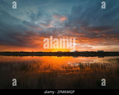 Cielo colorato e suggestivo del tramonto che si riflette sull'acqua dello stagno. Scena serale silenziosa al lago Delia. Nuvole al tramonto all'orizzonte sulla città di Ungheni Foto Stock