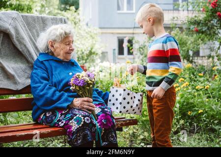 bisnonna di 90 anni, nonna con nipote insieme. Nipote abbraccia la sua amata nonna. Il nipote di capretto è venuto alla nonna con il fiore Foto Stock