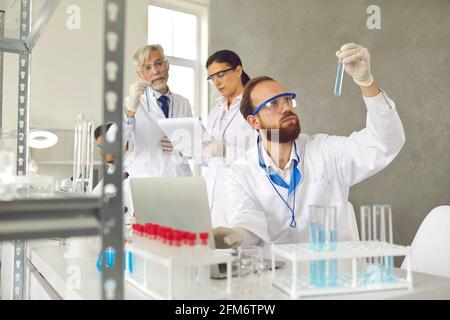 Concentrarsi sul lato anteriore di uno scienziato maschile del portatile che tiene il tubo di prova matraccio in laboratorio Foto Stock