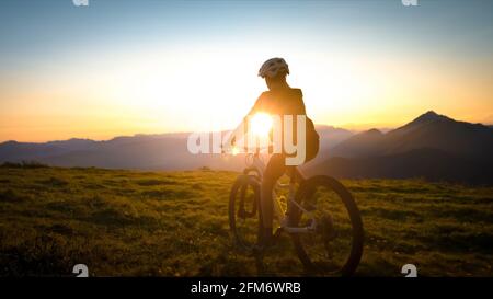 Bambina in mountain bike al tramonto. Bella luce dorata estiva. Foto Stock