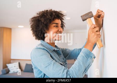 Donna afro che batte chiodo sul muro a casa. Foto Stock