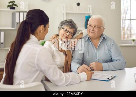 Felice coppia anziana che parla con il medico di famiglia seduto al tavolo presso l'ufficio del medico Foto Stock