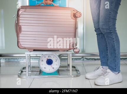 Mano femmina che tiene il peso della valigia sui chilo scale per controllare il peso preparare il check-in al terminal dell'aeroporto. Foto Stock