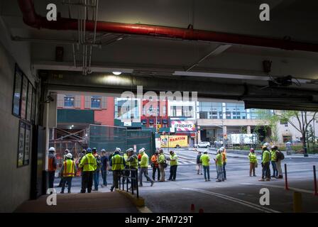 Un grande gruppo di costruttori che indossano una protezione personale aspetta in strada per iniziare il loro lavoro. Foto Stock