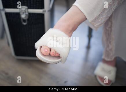 Un piede femminile con una scarpetta bianca di furry che dice sposa mentre ha le gambe incrociate indossare pigiami Foto Stock