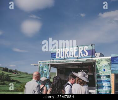 gli ospiti in fila per un matrimonio al furgone esterno con catering per hamburger in estate sotto il cielo blu Foto Stock