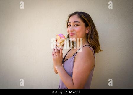 Petite giovane donna asiatica realisticamente mangiare Arcobaleno Sherbet gelato In un cono waffle in ambiente urbano Foto Stock