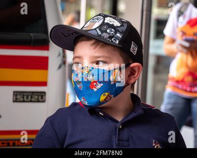 Medellin, Antioquia, Colombia - 3 aprile 2021: Piccolo ragazzo latino vestito in blu alla stazione degli autobus fissando con maschera COVID viso Foto Stock