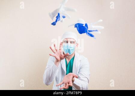 Giovane medico ritratto in bianco camice da laboratorio maschera protettiva di respirazione getta giù guanti bianchi e blu su sfondo giallo isolato. Foto Stock