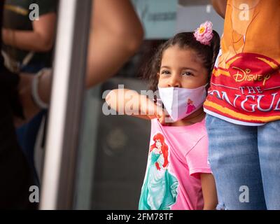 Medellin, Antioquia, Colombia - 3 aprile 2021: Ragazza ispanica piccola vestita in rosa alla stazione degli autobus fissando con maschera COVID viso Foto Stock