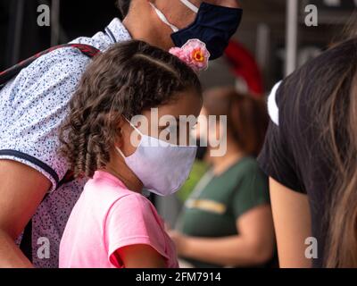 Medellin, Antioquia, Colombia - 3 aprile 2021: Ragazza ispanica piccola vestito in rosa alla stazione degli autobus fissando tristemente con maschera COVID viso Foto Stock