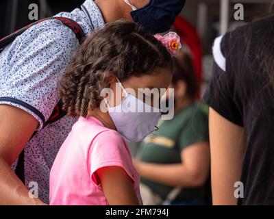 Medellin, Antioquia, Colombia - 3 aprile 2021: Ragazza ispanica piccola vestito in rosa alla stazione degli autobus fissando tristemente con maschera COVID viso Foto Stock