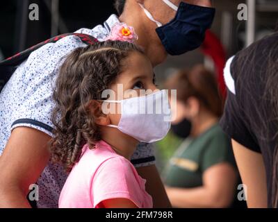 Medellin, Antioquia, Colombia - 3 aprile 2021: Ragazza ispanica piccola vestita in rosa alla stazione degli autobus fissando con maschera COVID viso Foto Stock