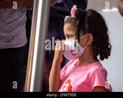 Medellin, Antioquia, Colombia - 3 aprile 2021: Ragazza ispanica piccola vestita in rosa alla stazione degli autobus fissando con maschera COVID viso Foto Stock