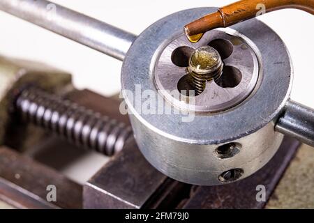 Taglio della filettatura nella vite durante il funzionamento. Gocce di olio dall'oliatore sul coltello per tagliare le filettature. Sfondo isolato. Foto Stock