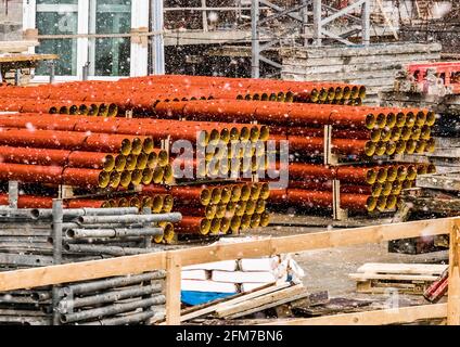 Cumulo di tubi termoplastici in polietilene industriale rotondi stoccaggio all'aperto in un cantiere con neve in inverno freddo. Foto Stock