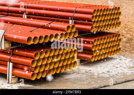 Cumulo di tubi termoplastici in polietilene industriale rotondi stoccaggio all'aperto in un cantiere con neve in inverno freddo. Foto Stock