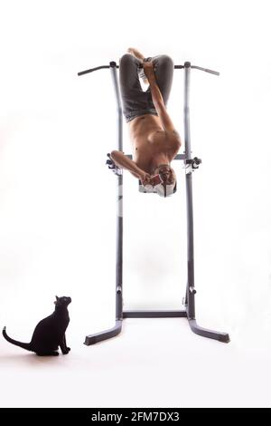 Un uomo tiene la macchina fotografica capovolta su una macchina di esercitazione, isolata su uno sfondo bianco.UN gatto nero seduto guardando un uomo Foto Stock