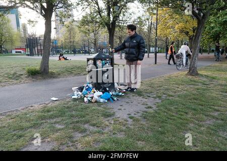 Un uomo mette una bottiglia vuota in un bidone già pieno in un parco. Le persone si affollano in spazi all'aperto fino a quando non è consentito socializzare al coperto ancora una volta Foto Stock