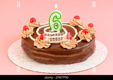 Torta di cioccolato di compleanno con candela bruciante sotto forma di numero sei. Torta fatta in casa decorata con crema di cioccolato e ciliegie primo piano sul retro rosa Foto Stock