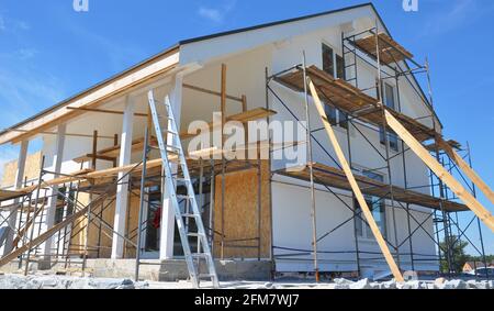 Moderna riparazione e ristrutturazione della casa. Intonacatura, applicazione di stucco e verniciatura delle pareti della facciata utilizzando ponteggi durante la ristrutturazione della casa. Foto Stock