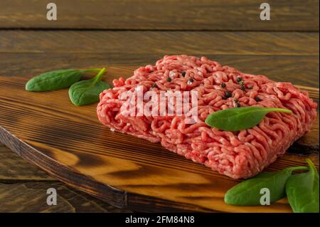 Carne di manzo macinata grezza su un tagliere di legno con verdure e spezie. Concetto di cucina e di alimentazione sana Foto Stock