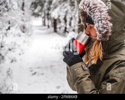 Il tè mantiene la ragazza calda all'esterno. Giovane donna che ama la bevanda calda in inverno. Abete rosso albero Foresta coperta da neve in inverno Paesaggio sullo sfondo . immagine per sfondo. Spazio di copia Foto Stock