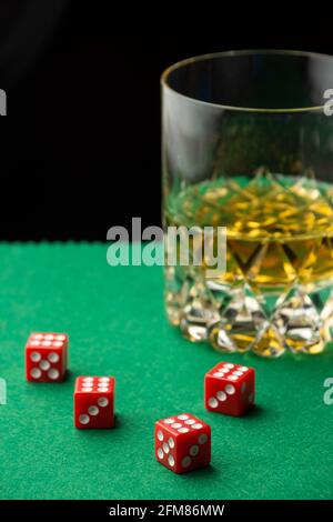 Vista dall'alto di dadi rossi su baize verdi con bicchiere di whisky, sfocati, fondo nero, verticale, con spazio per la copia Foto Stock