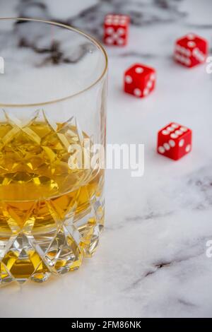 Vista dall'alto di vetro con whisky su marmo bianco, con dadi rossi, sfocati, in verticale, con spazio per la copia Foto Stock