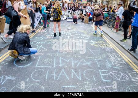 Gli studenti dell'università di Bath e i bambini della scuola sono raffigurati scrivendo slogan sulla strada mentre prendono parte ad una marcia di protesta del cambiamento climatico a Bath