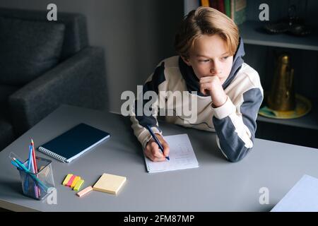 Mani ravvicinate di pupillo che scrive nel notebook risolvendo equazioni matematiche seduti alla scrivania a casa. Foto Stock