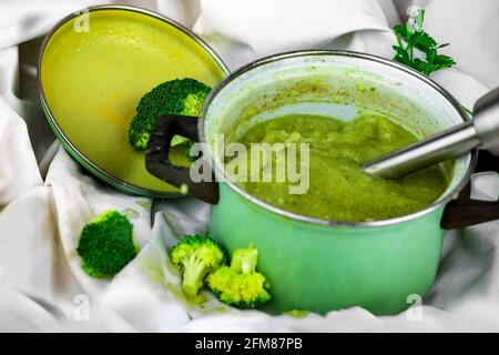 Frullatore a immersione in pentola verde con zuppa di broccoli su fondo bianco. Preparazione di zuppa di broccoli vegetariana. Foto Stock