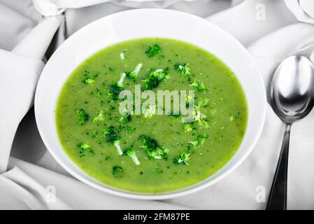 Zuppa di broccoli di colore verde fresco in piastra bianca, cucchiaio su fondo bianco di tovaglia. Foto Stock