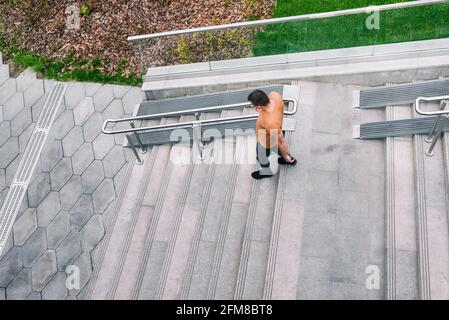 L'uomo scende le scale. Scala in cemento con ringhiere e erba verde. Interni urbani. Vista dall'alto. Foto Stock