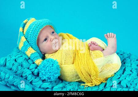 Bambino caucasico neonato dall'occhio blu con cofano a maglia sdraiato su un panno blu Foto Stock